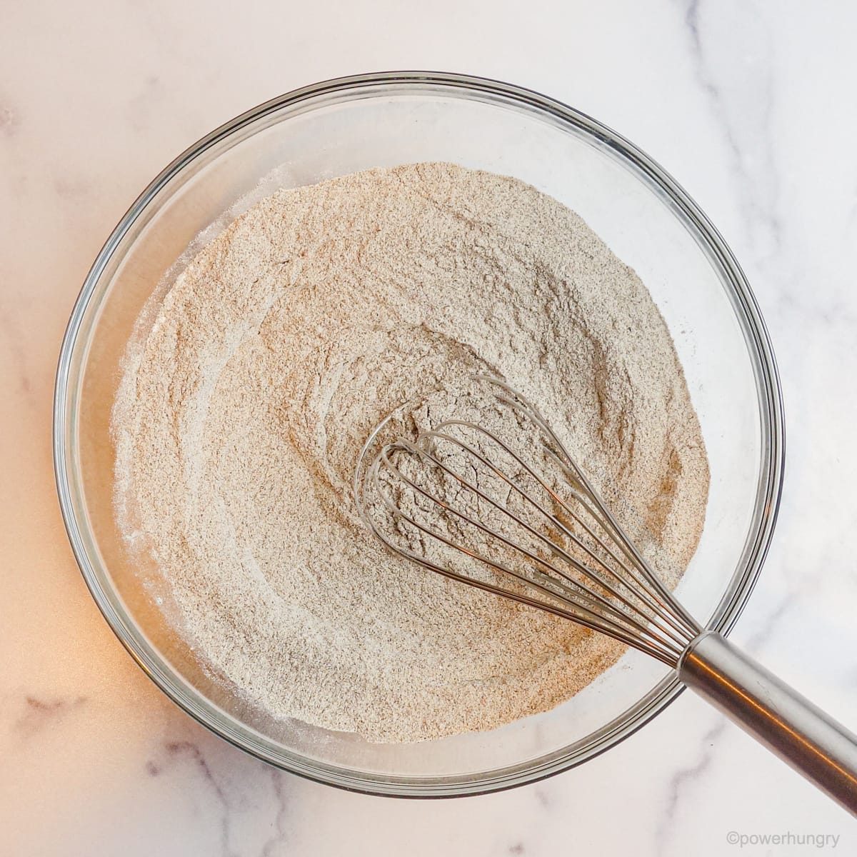 a glass bowl filled with buckwheat flour, baking powder, and salt with a metal whisk sticking out of the bowl