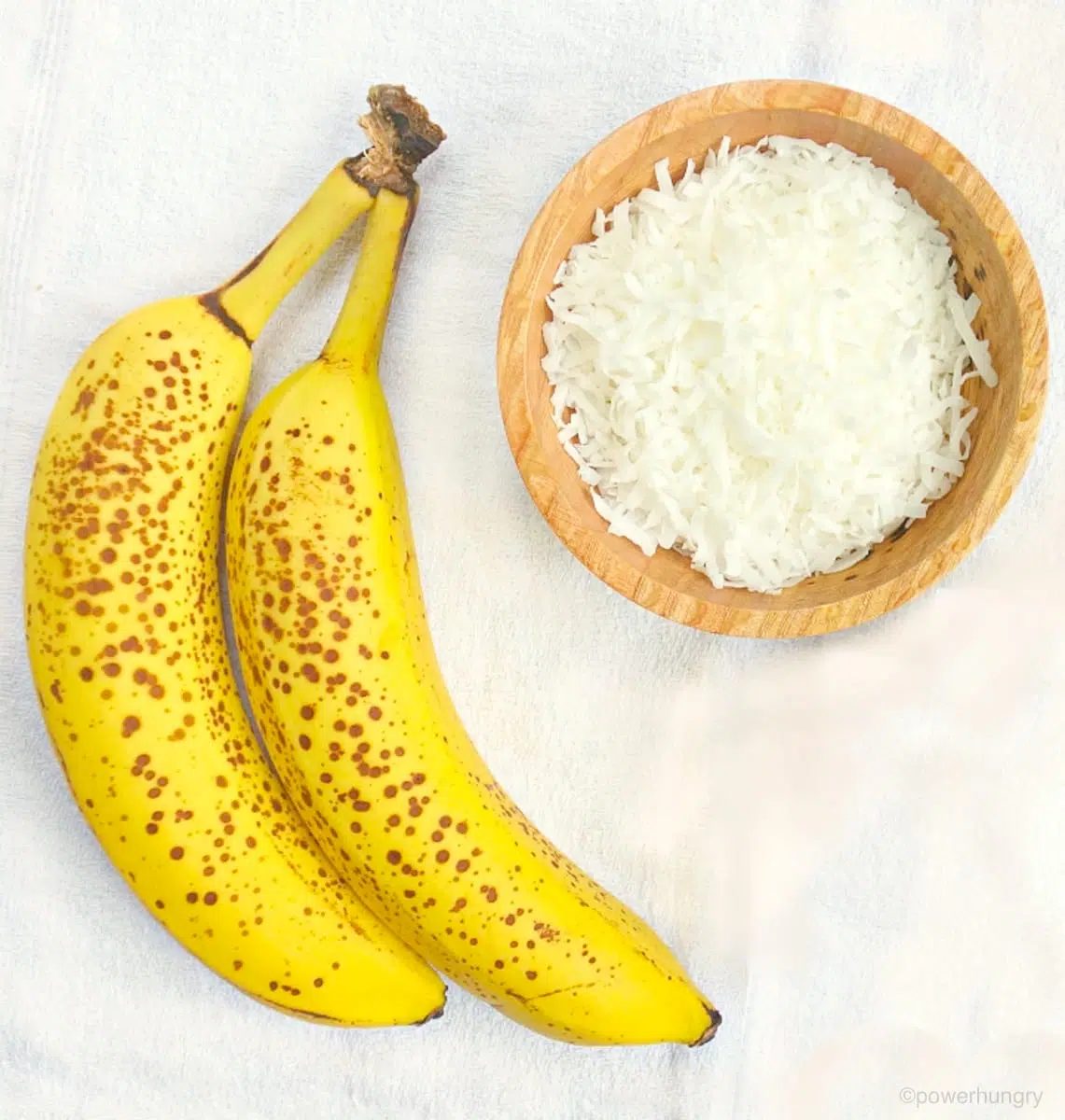 2 bananas and a bowl of shredded coconut on a white napkin