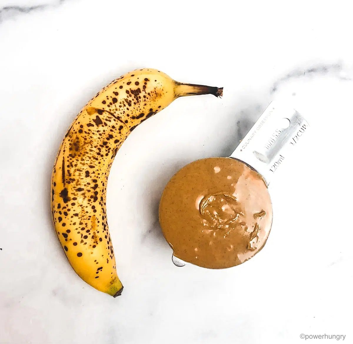 a ripe banana and a measuring cup full of natural peanut butter