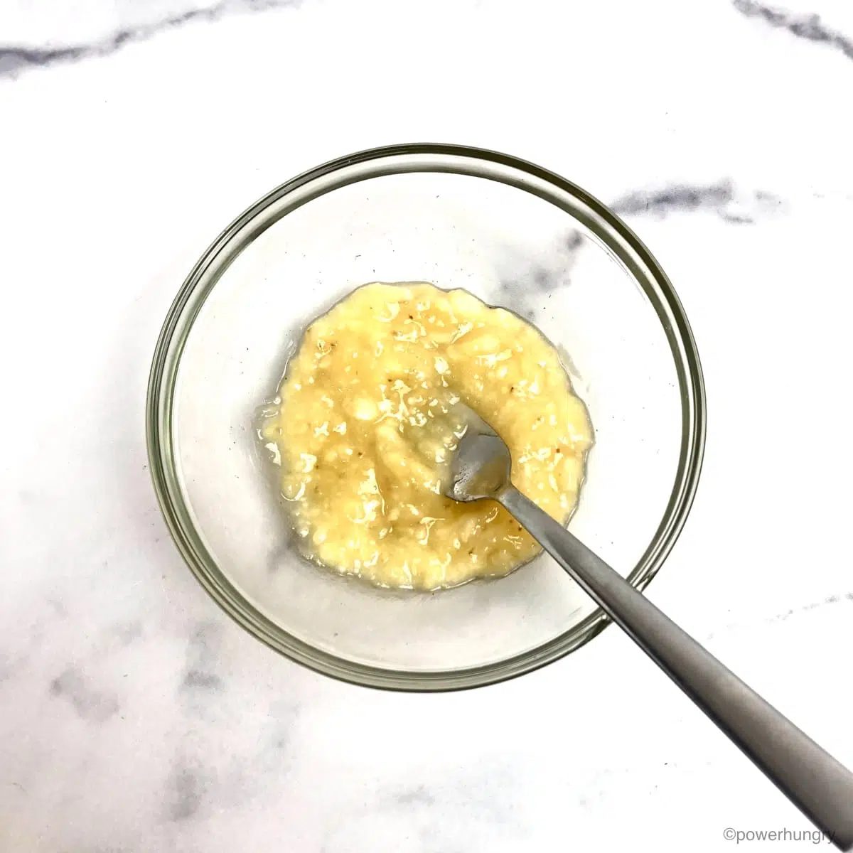 finely mashed banana in a glass bowl atop a white marble countertop