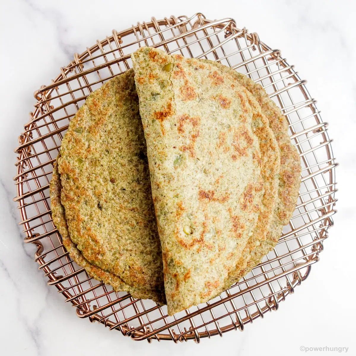 a folded pumpkin seed tortilla on top of a copper cooling rack