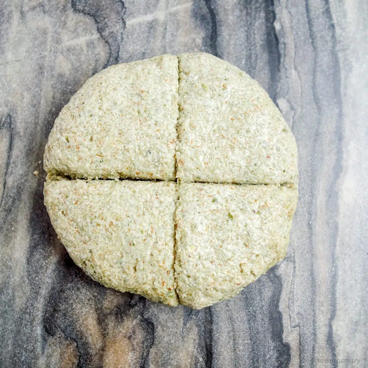 a disk of pepita tortilla dough on a grey marble cutting board, cut into quarters