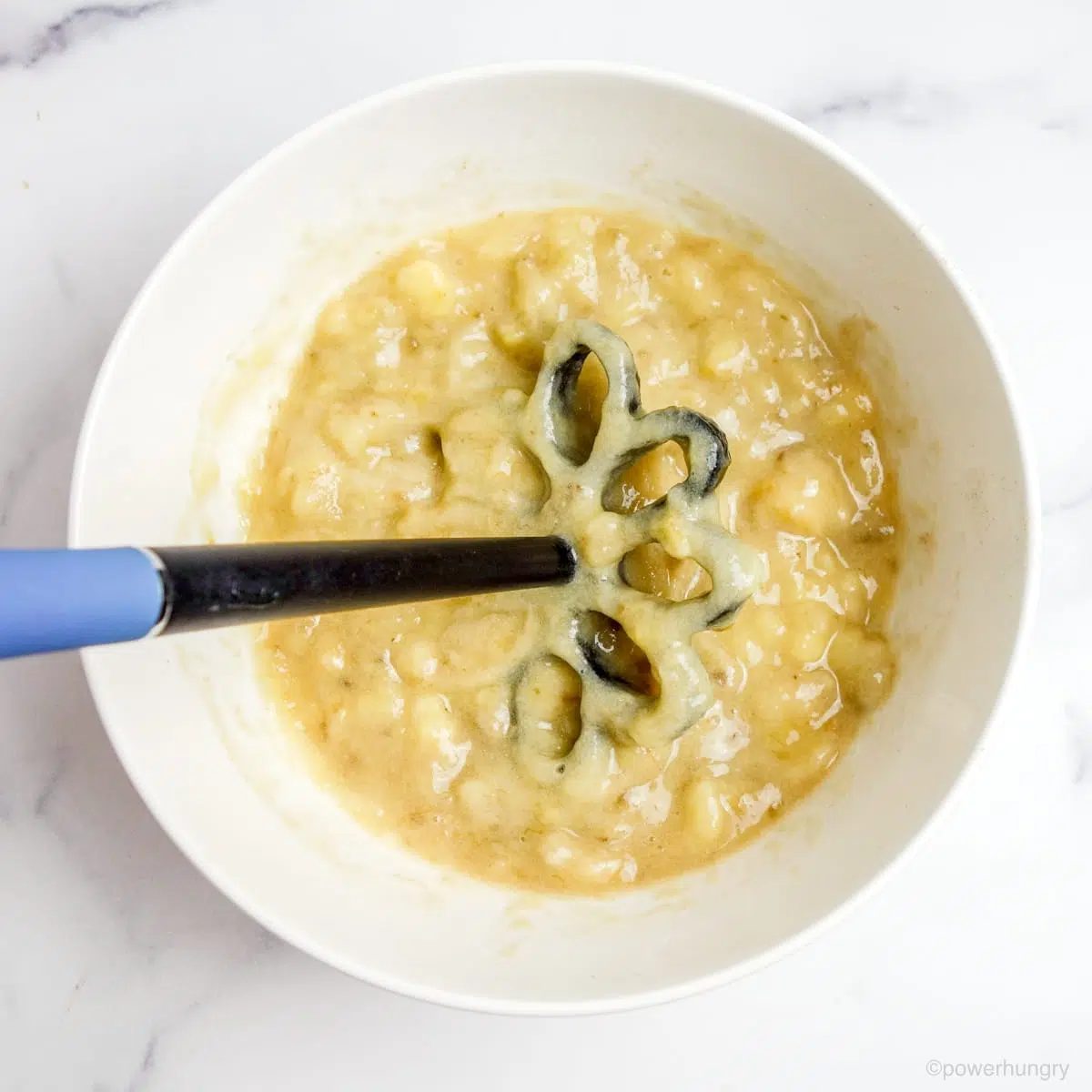 white bowl filled with finely mashed bananas and a masher