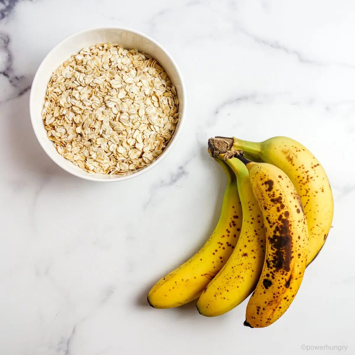 a white bowl filled with rolled oats and a pile of very ripe bananas