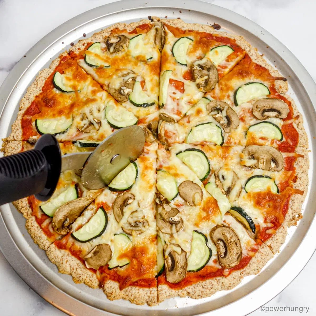 almond flour pizza crust, finished with topping, getting sliced with a pizza cutter