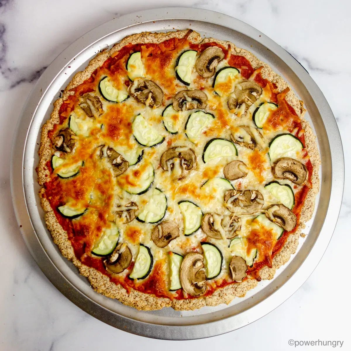 cooked 3 ingredient almond flour pizza crust topped with sauce, cheese, mushrooms and zucchini