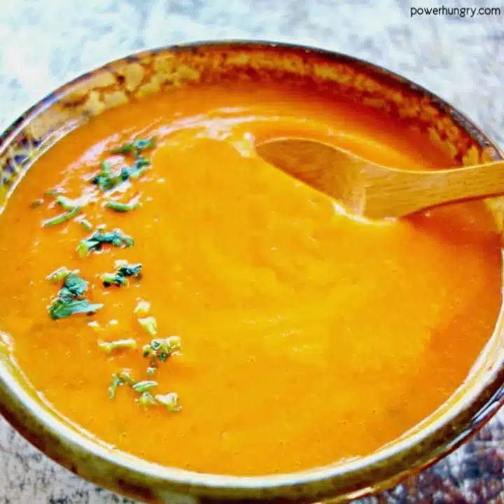 close-up of a vegan red lentil carrot soup in a potter bowl with a wooden spoon inserted