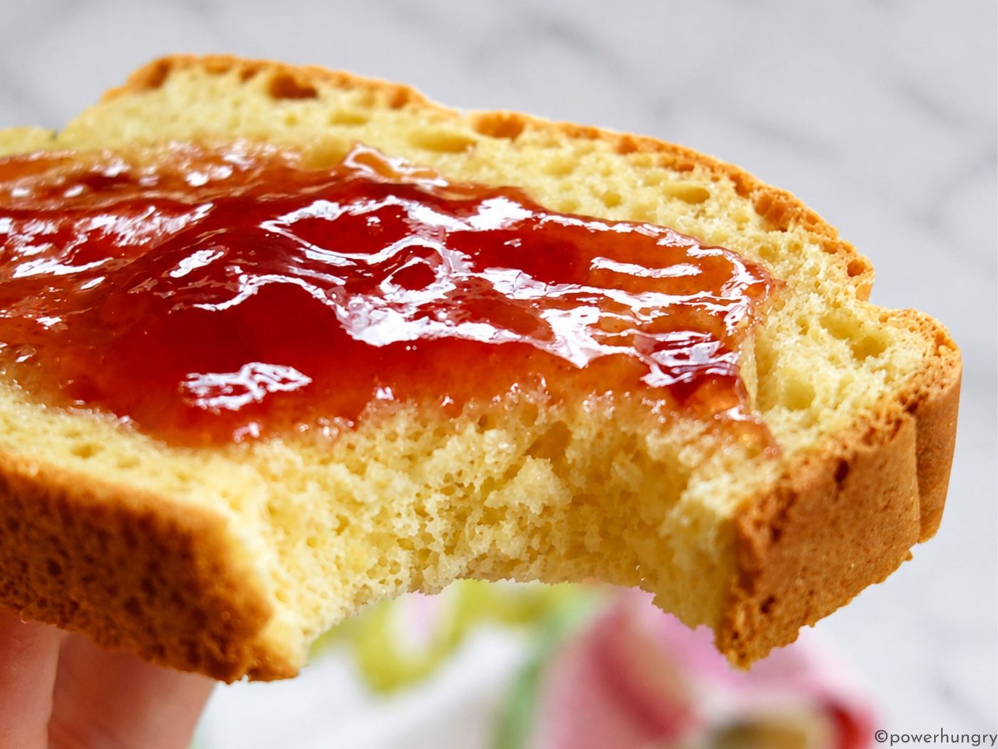 closeup of a slice of chickpea flour yeast-free bread, spread with jam, with a bite taken out