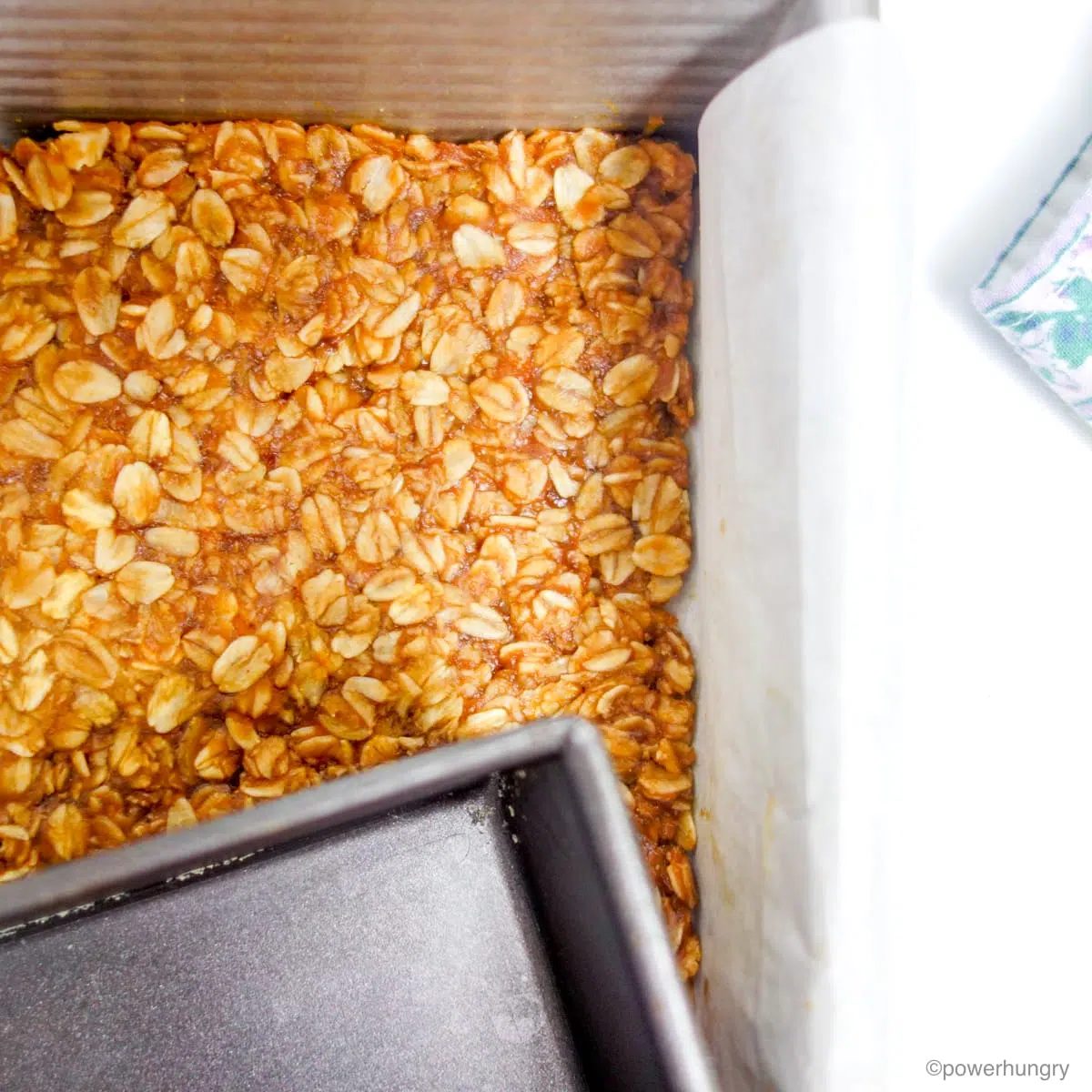 granola bar mixture getting pressed into a parchment paper lined baking pan