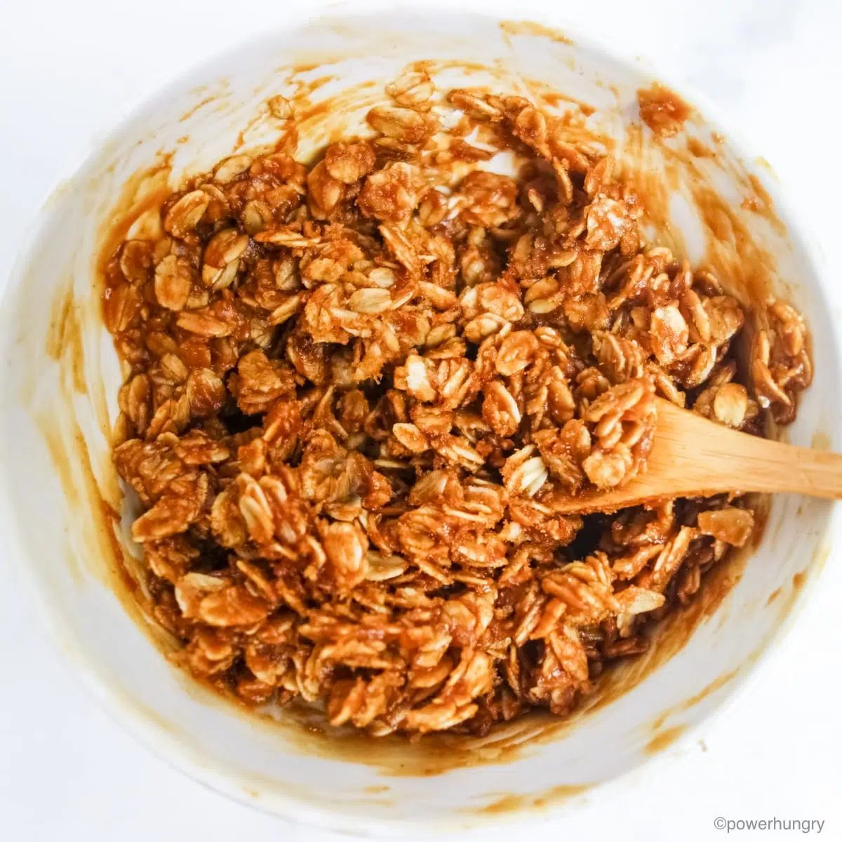no bake granola mixture in a white bowl with a wood spoon
