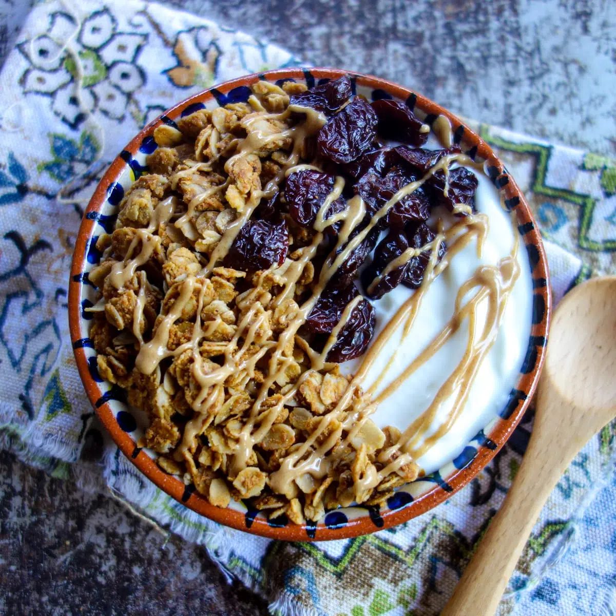 a bowl of yogurt topped with dried cherries, granola, and a drizzle of peanut butter.