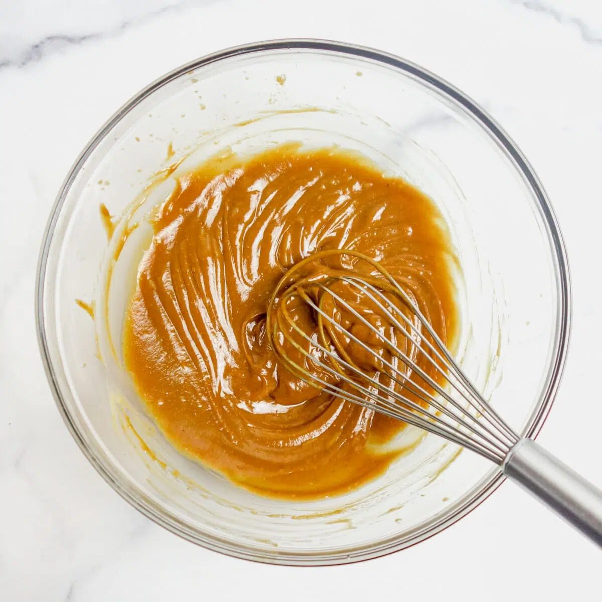 a glass bowl with whisked peanut butter and maple syrup