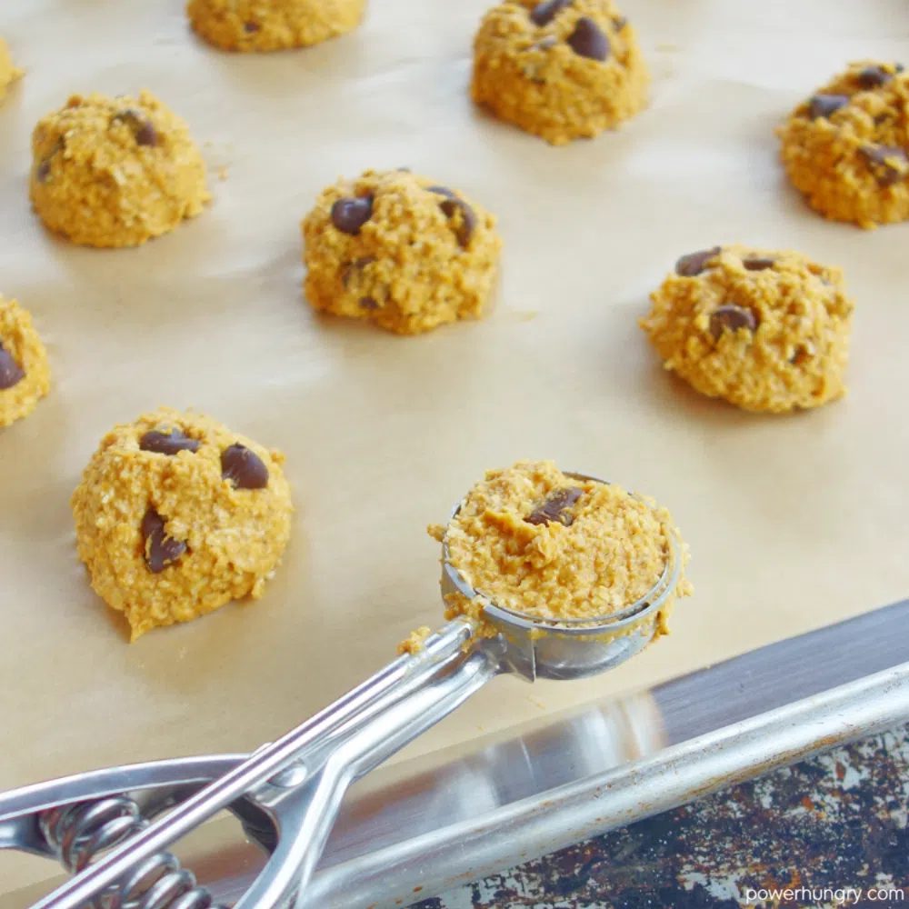 baking sheet with mounds of cookie dough and a cookie scoop in the foreground