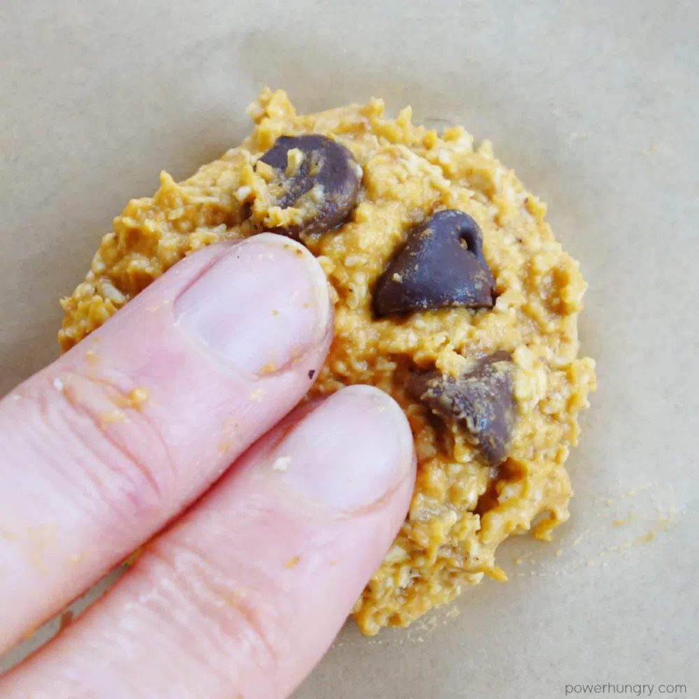 close up of a mound of pumpkin cookie dough being flattened with fingertips