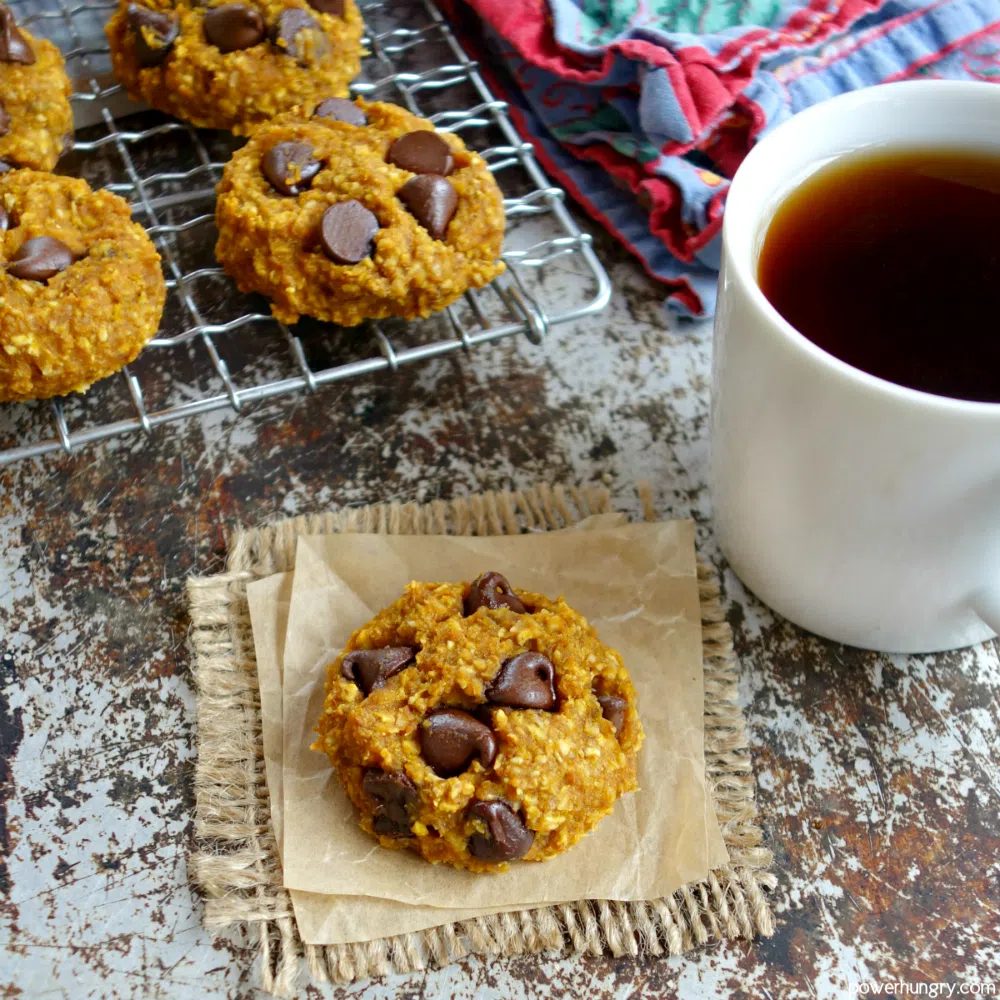 pumpkin cookie on a piece of brown parchment with more cookies on a rack in the background