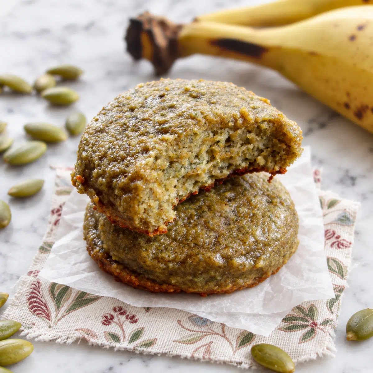 two pumpkin seed flour banana cookies stacked, with one bitten