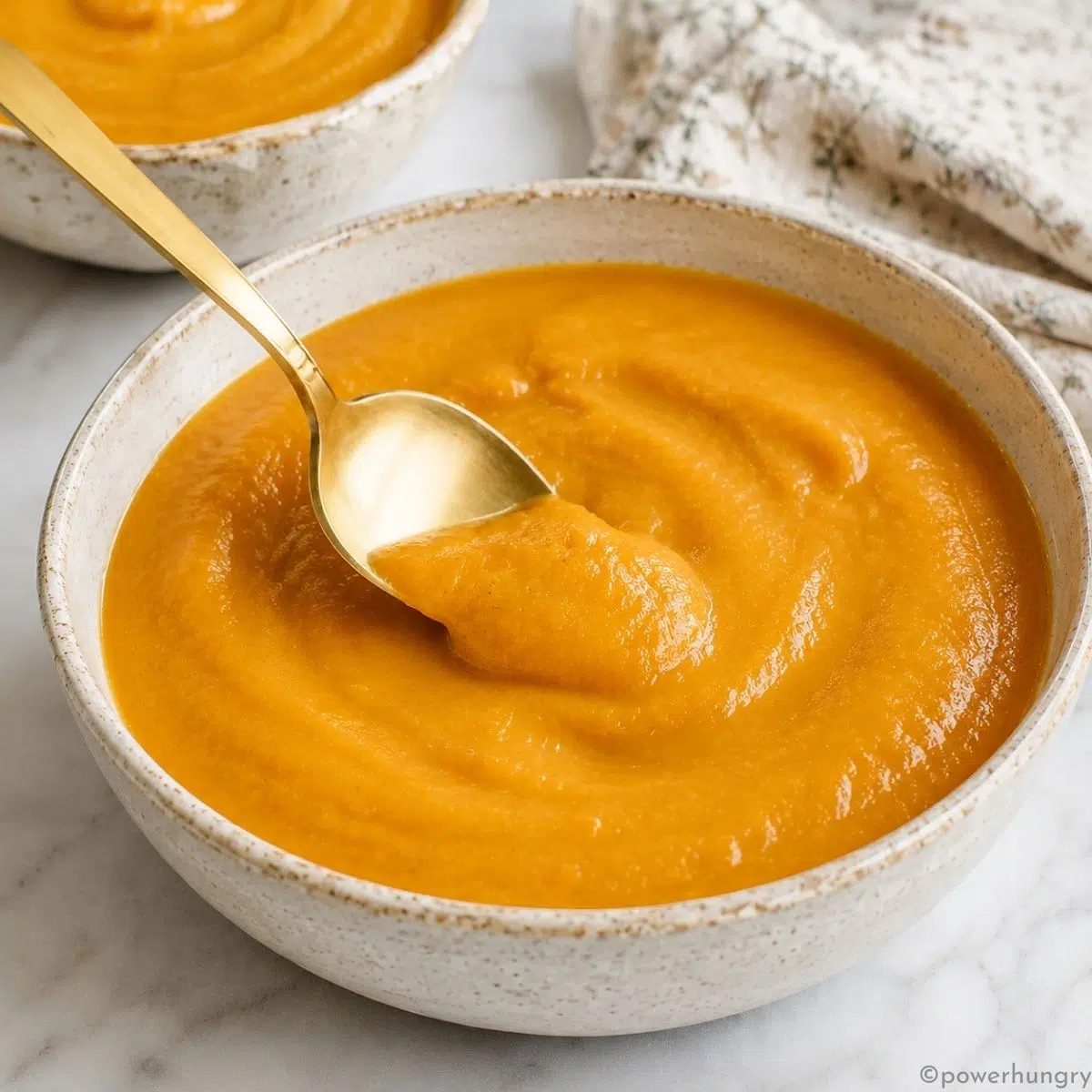 bowl of roasted carrot soup with a matte gold soup spoon spooning up some of the soup
