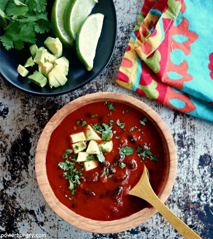 overhead shot of 3-Ingredient Vegan Enchilada Soup in a wooden bowl with a wooden spoon. Soup topped with avocado and cilantro