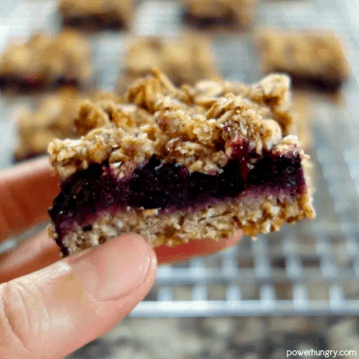 A hand holding a cut blueberry oat bar, showing the thick fillling