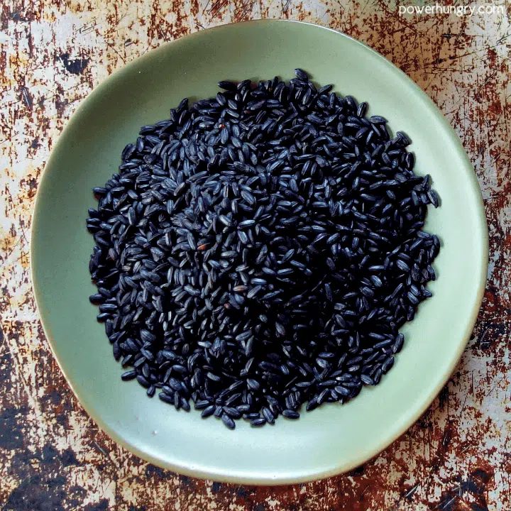 uncooked grains of black rice on a sage green dish