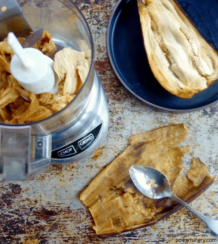 roasted eggplant being scraped from its skin to be processed in a food processor