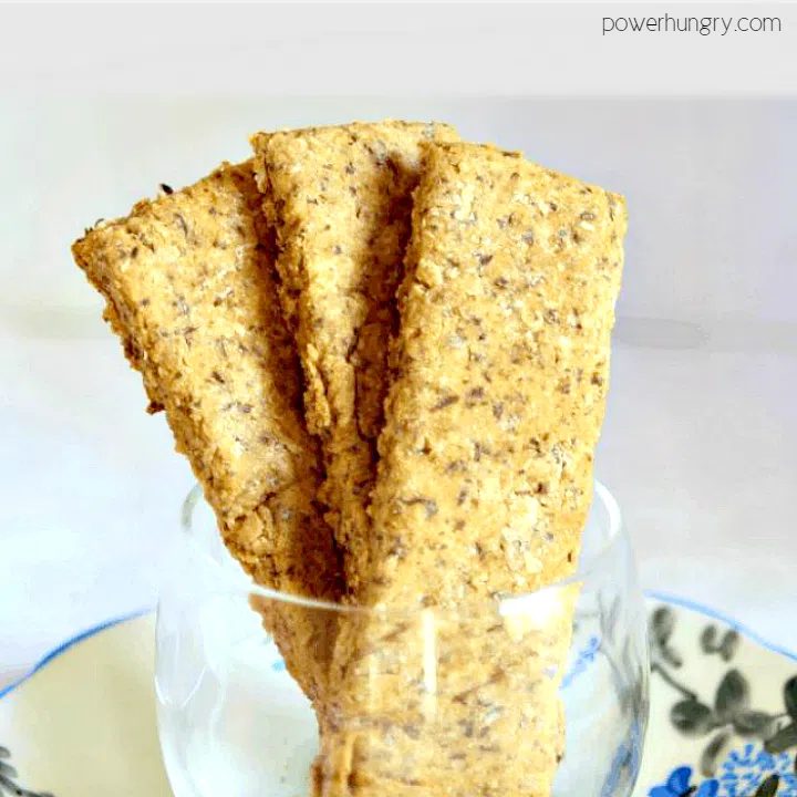 almond oat chickpea flour crackers stacked in a glass cup atop a white and blue plate