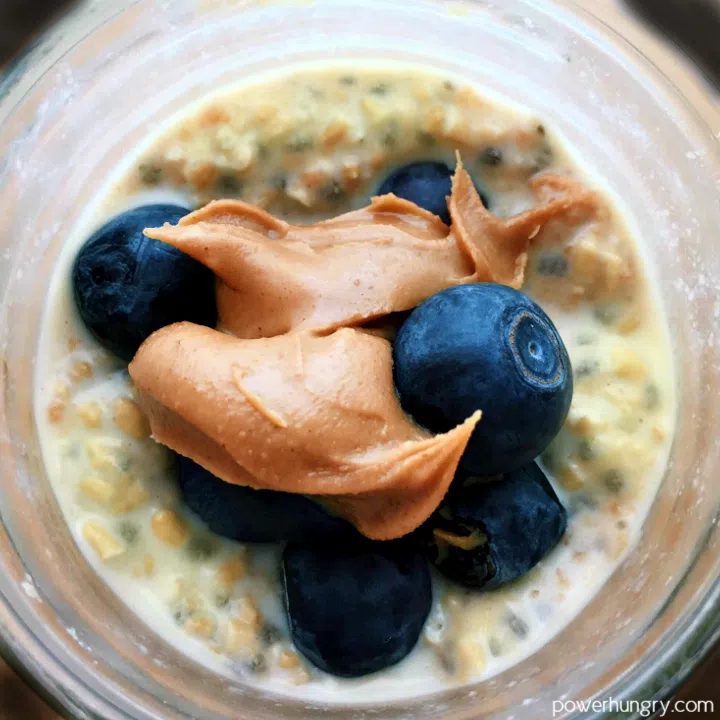 overhead sot of banana chia overnight oats in a glass jar, topped with blueberries and almond butter