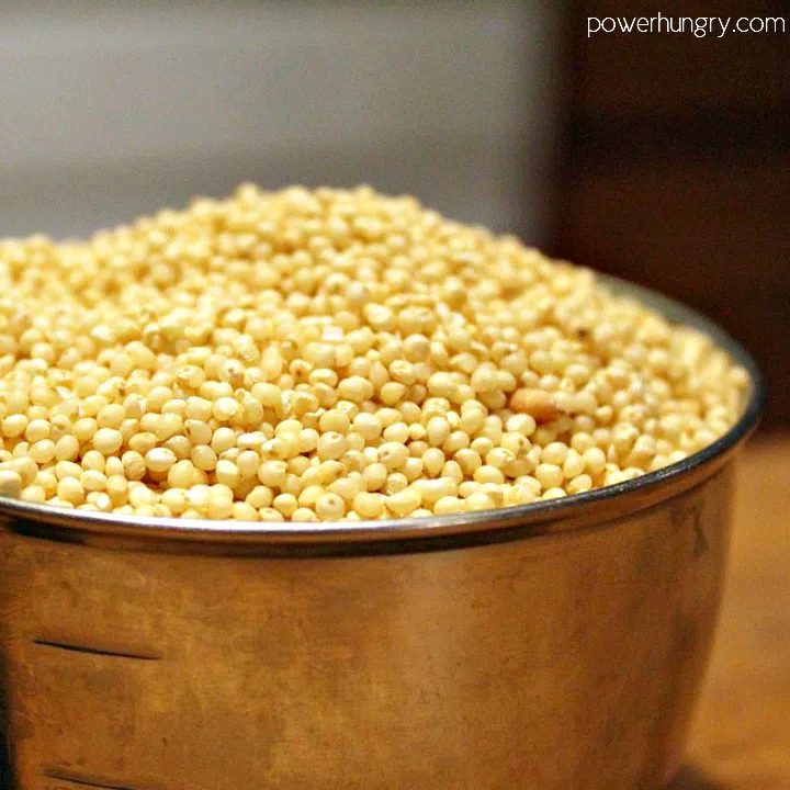 a metal measuring cup filled to the brim with uncooked millet.