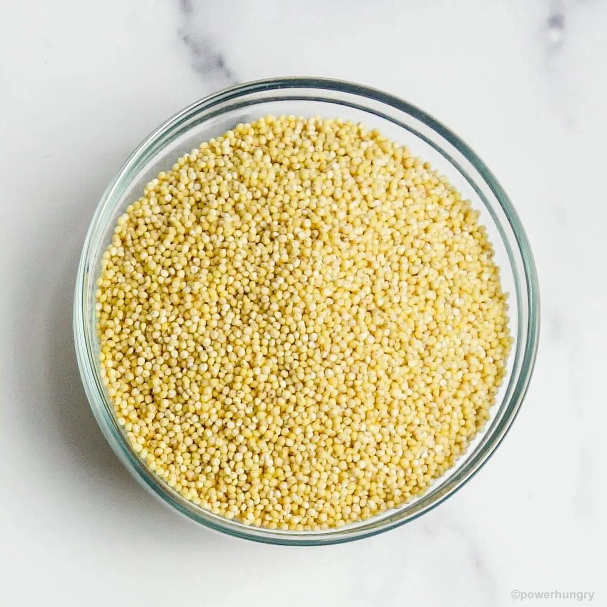 glass bowl of raw millet on a marble countertop