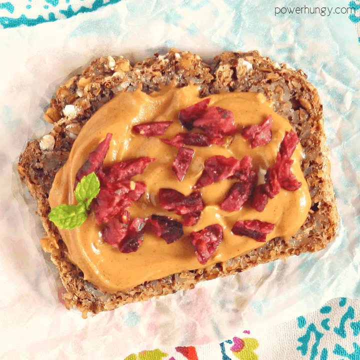 overhead close-up shot of buckwheat flax chia bread topped with nut butter and dried cranberries