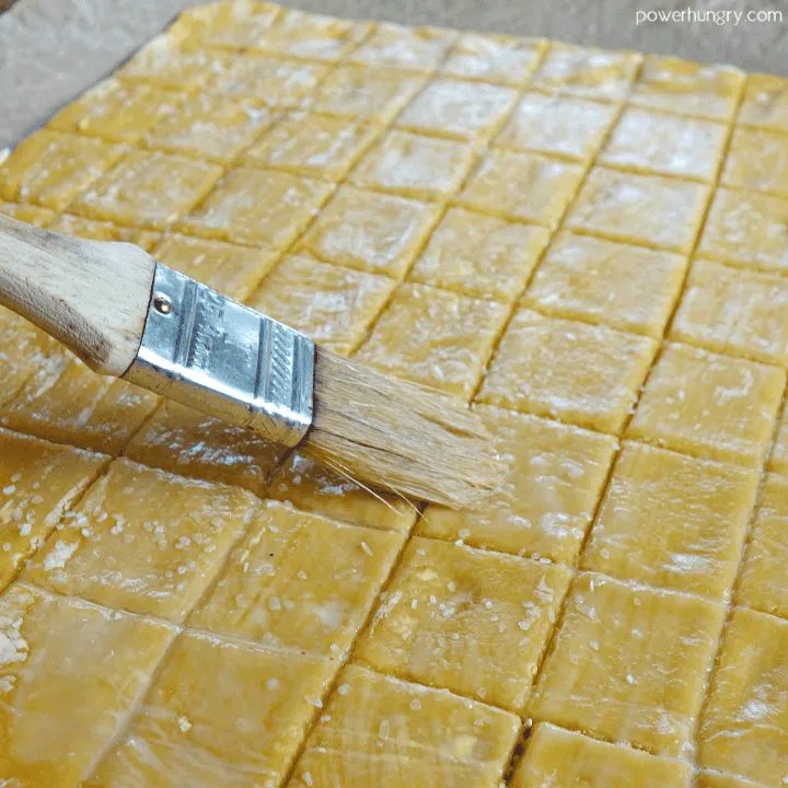 unbaked cheese-y chickpea flour crackers being brushed with water