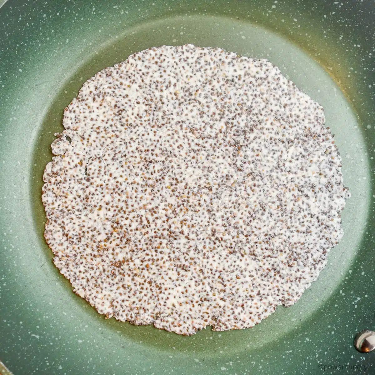 an uncooked coconut flour tortilla in a green nonstick skillet