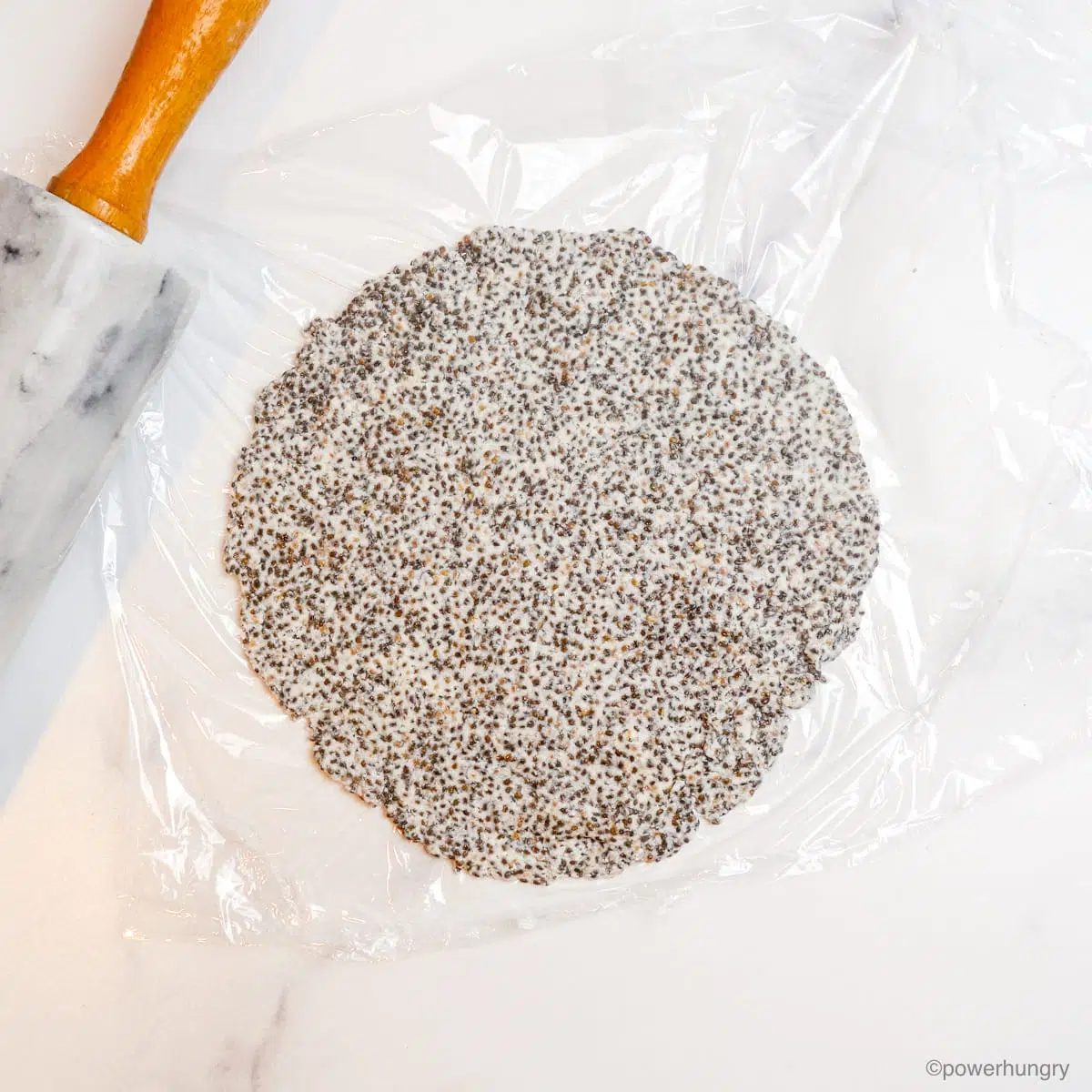 a rolled out chia tortilla, in between two pieces of plastic wrap