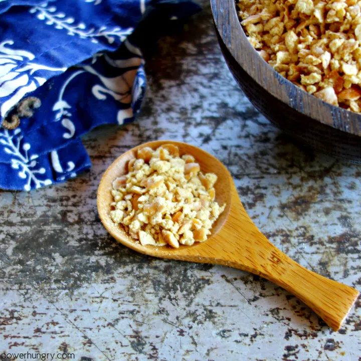 a wooden spoon filled with chickpea breadcrumbs , with a bowl of the crumbs and a navy napkin in the background
