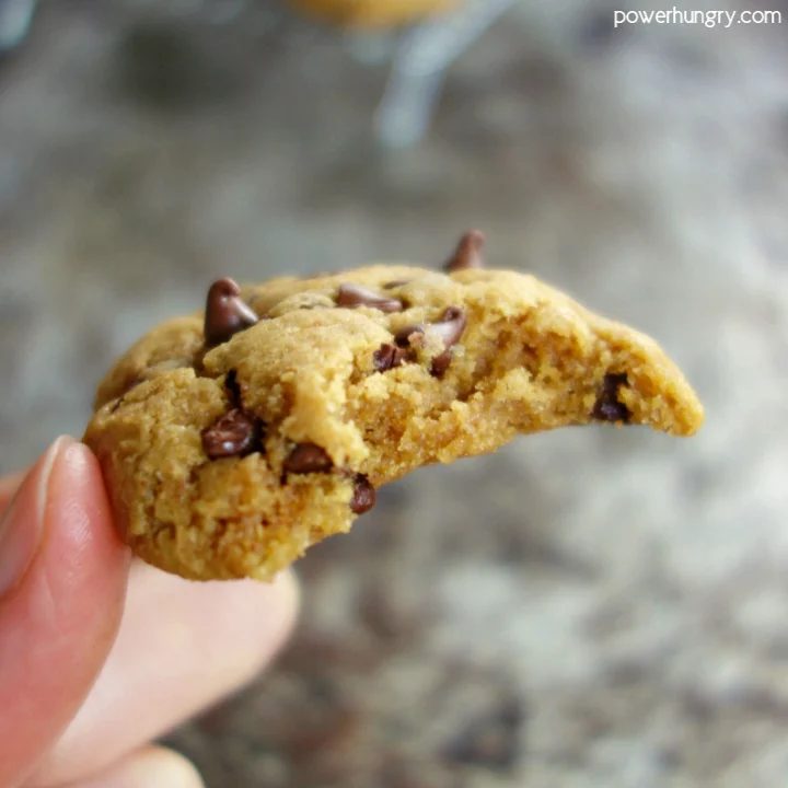 a hand holding a chickpea flour chocolate chip cookie with a bite taken out of it