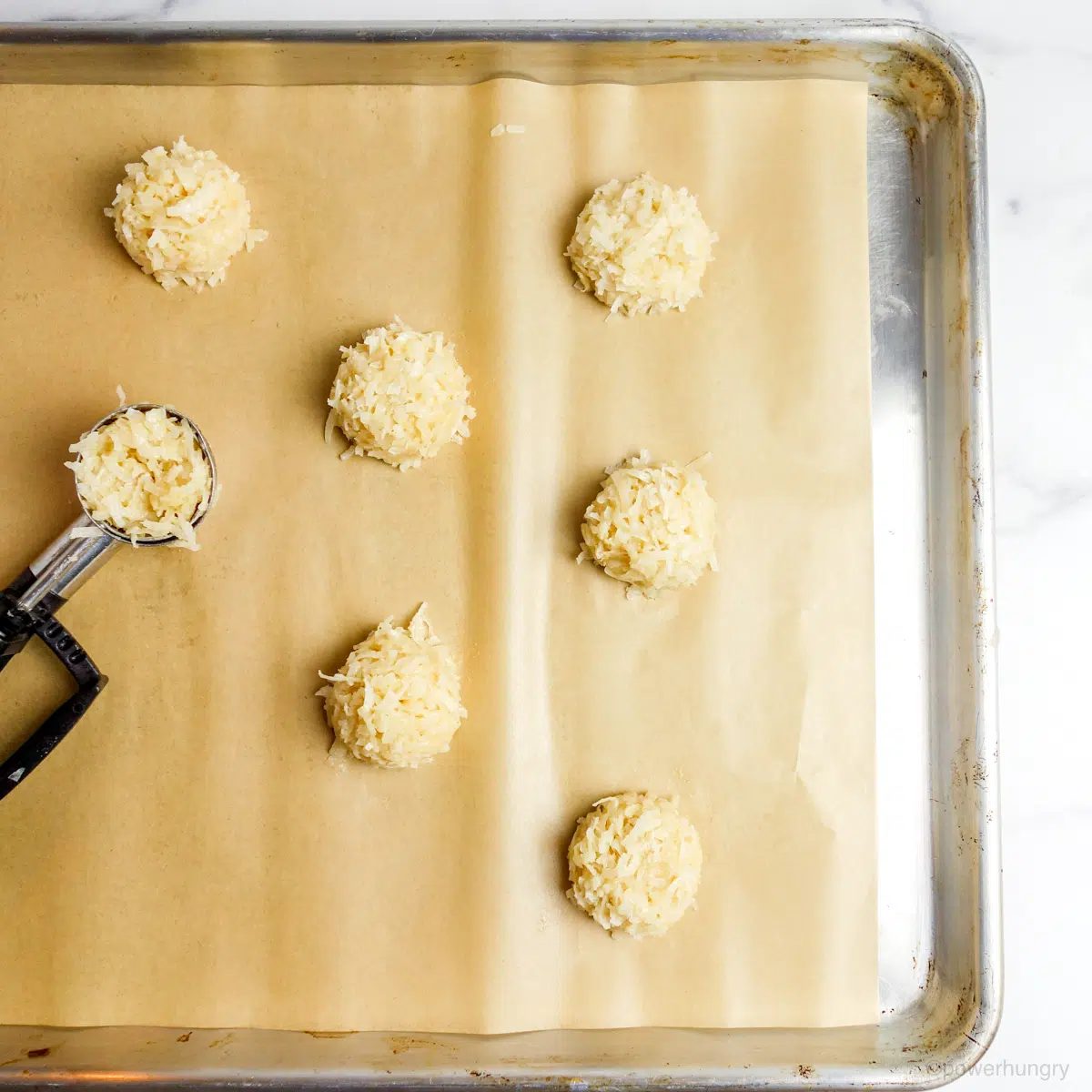 vegan coconut macaroon dough portioned onto a parchment lined baking sheet.