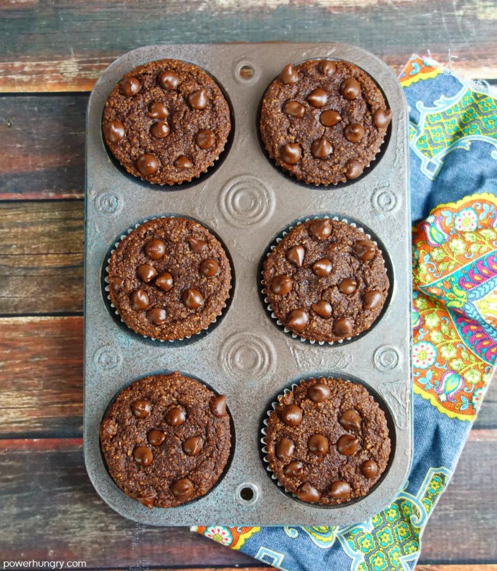 6chocolate muffins in an antique muffin tin, set on top of a wooden board with a colorful napkin alongside