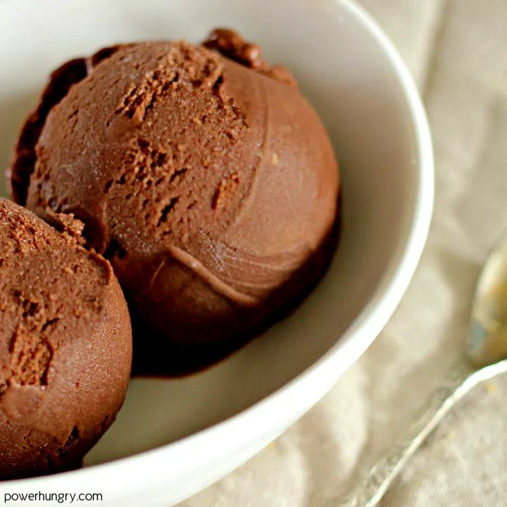 close up of a scoop of chocolate avocado ice cream in a white dish with a white background