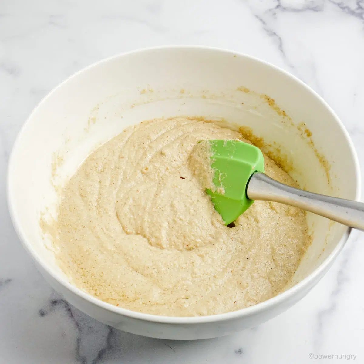 white bowl with a green silicone spatula showing the mixed batter for coconut flour oat blueberry muffins