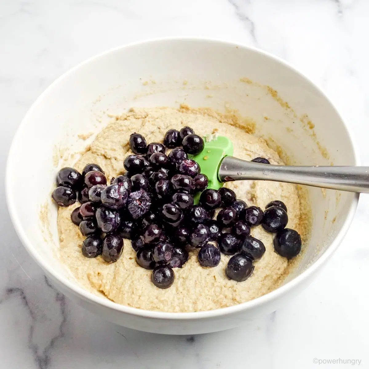 coconut flour oat muffin bater in a white bowl with blueberries on top