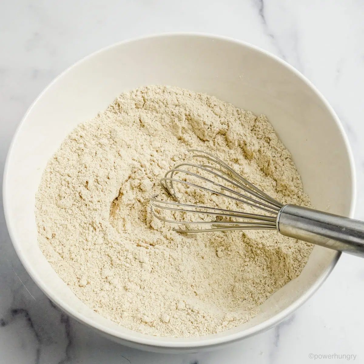 white bowl filled with whisk and dry ingredients for coconut oat muffins