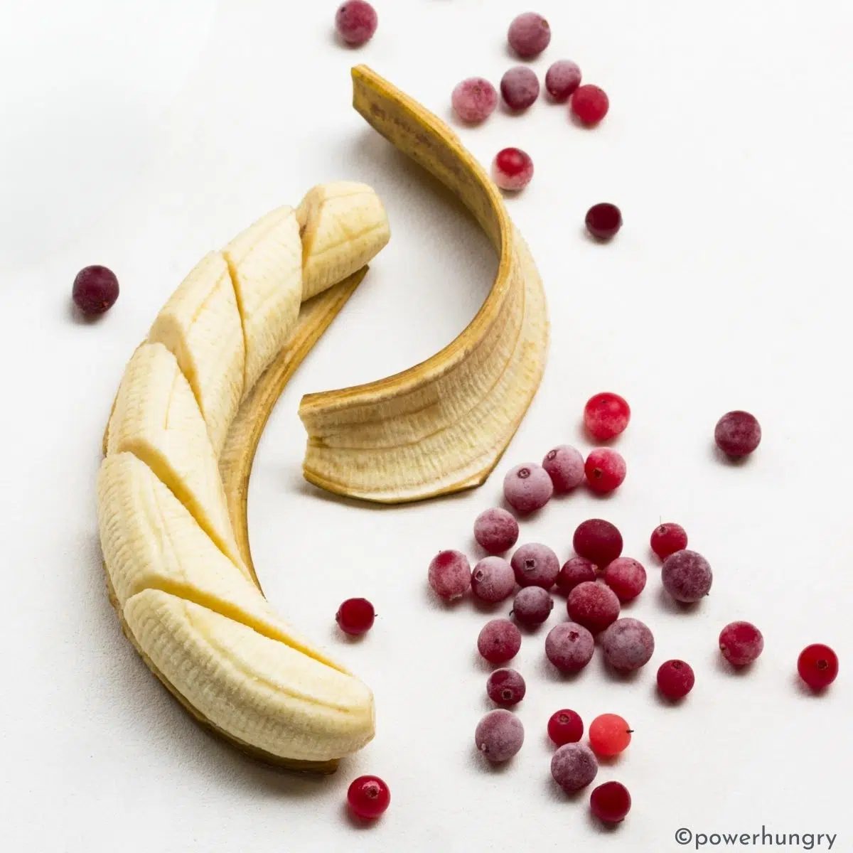banana and frozen cranberries on a white surface