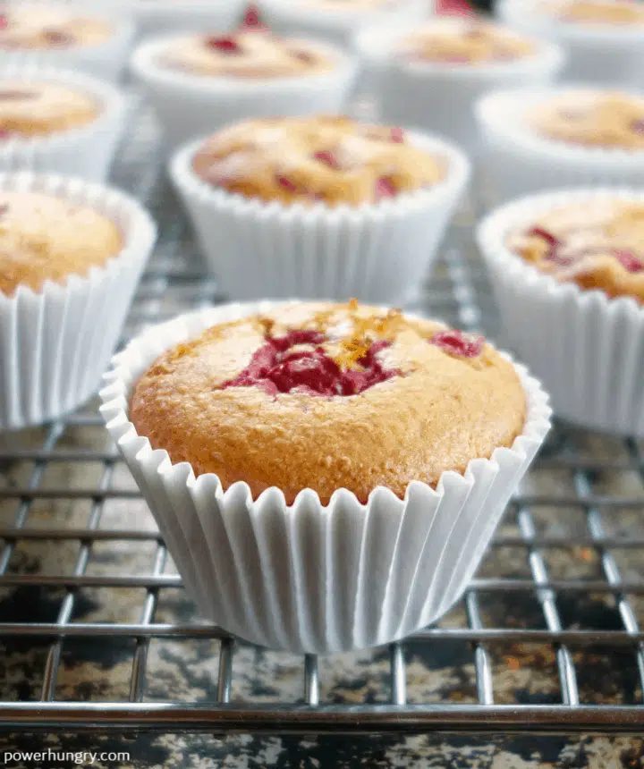 close up of a cranberry orange chickpea flour muffin on a wire cooling rack, with more muffins in the background