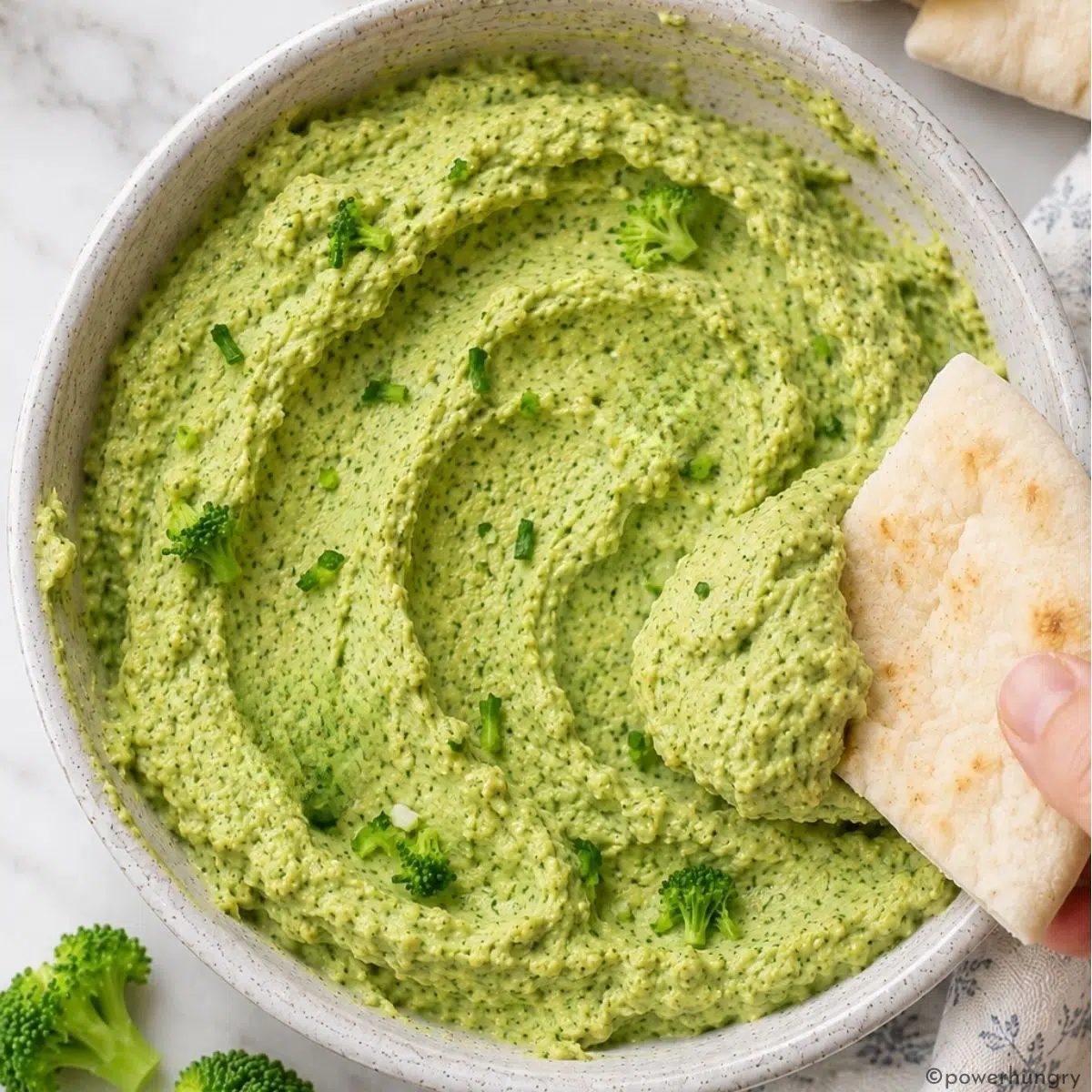 overhead shot of broccoli hummus with my hand shown dipping in some pita bread