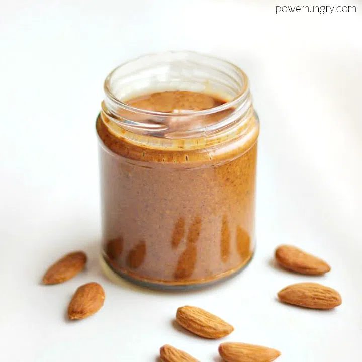 jar of kitchen-made almond butter surrounded by some whole almonds