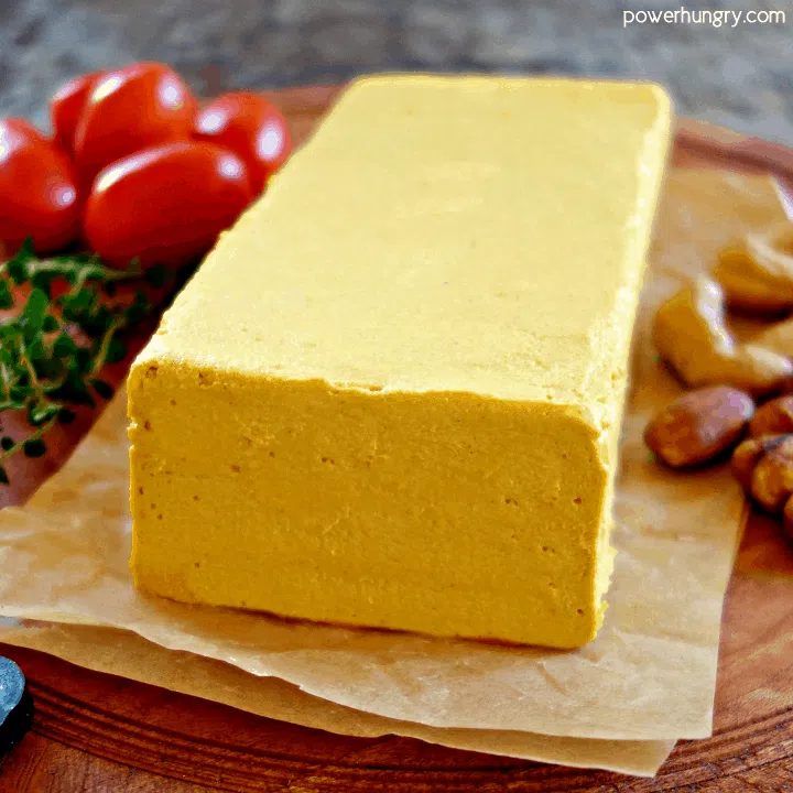 Loaf of cashew Cheddar cheese on parchment paper, atop a wooden cutting board