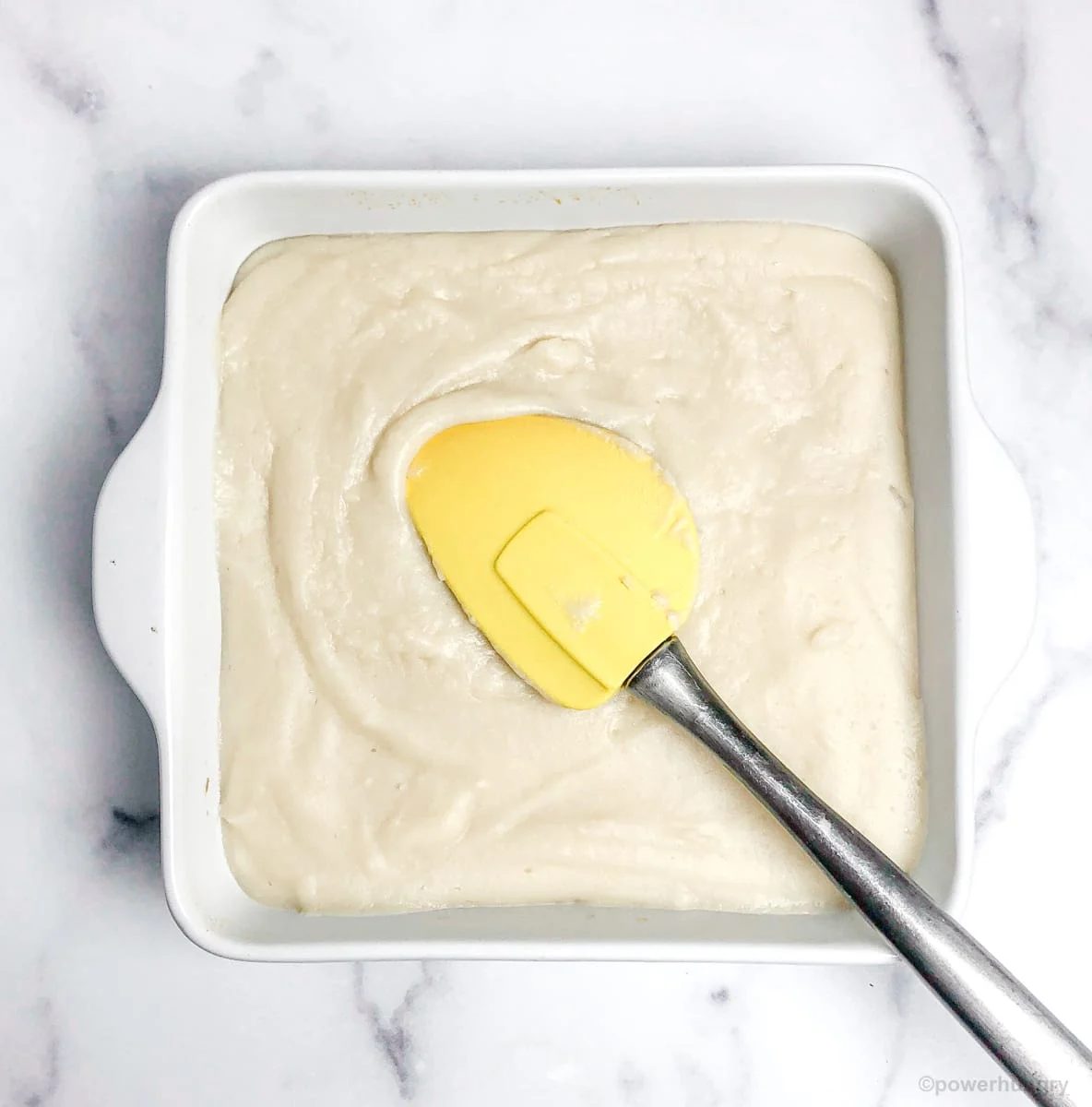 bean tofu batter being spread into an 8-inch white baking dish