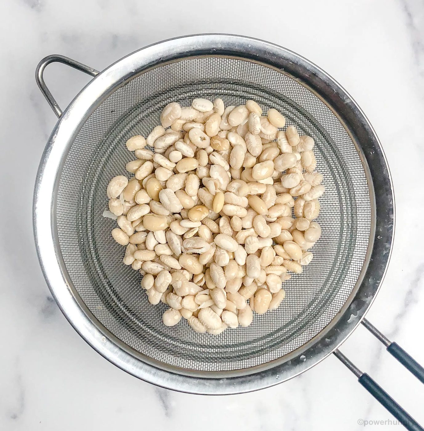 drained soaked white beans in mesh sieve