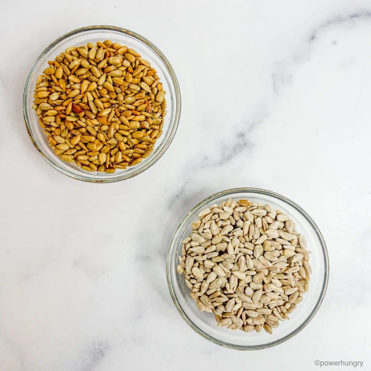 two glass bowls on a marble counter, each filled with sunflower seeds (raw and roasted)