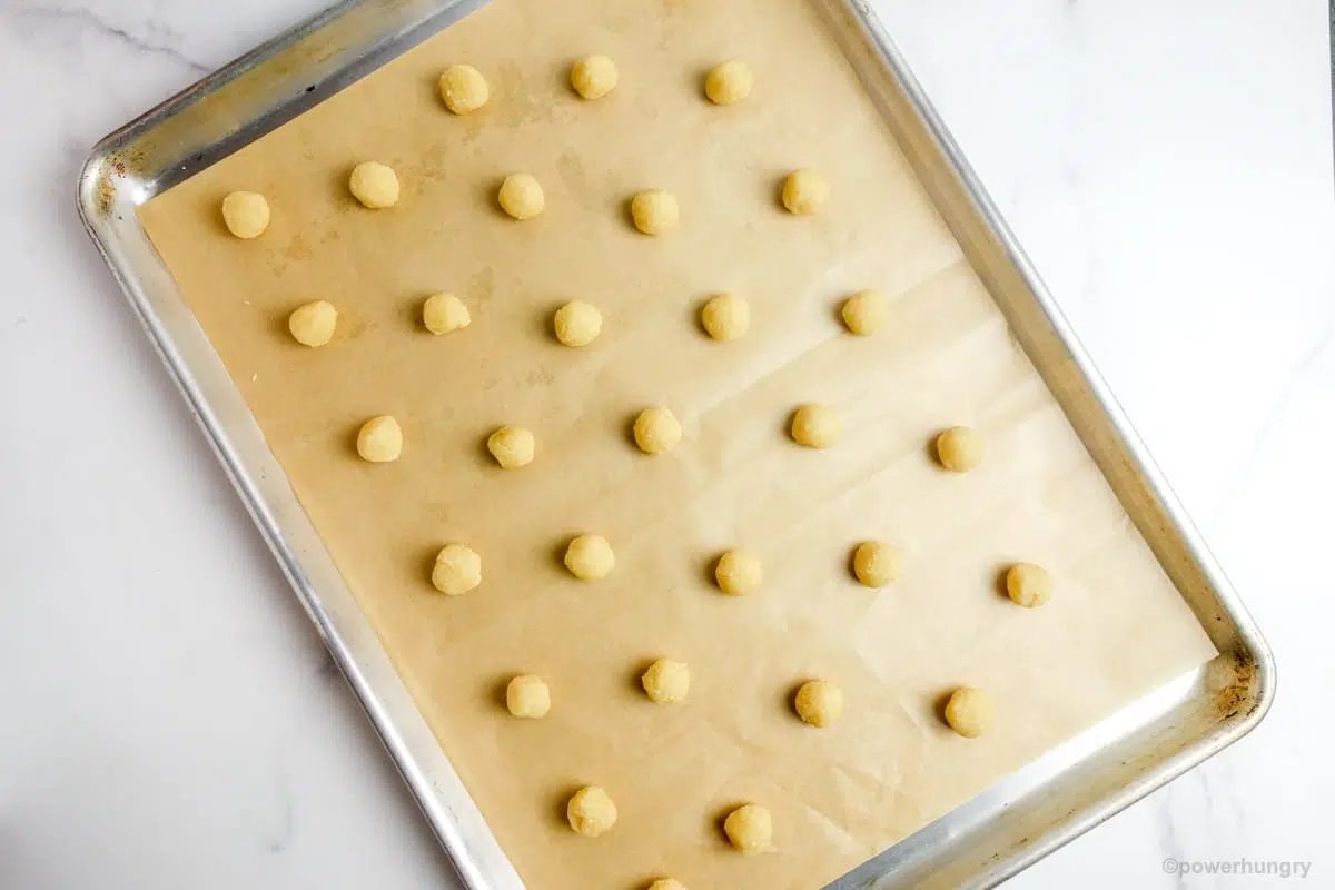 baking sheet covered with a piece of brown parchment paper and 32 almond flour dough balls